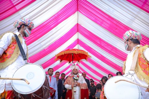 Free Vibrant Indian wedding procession with traditional drummers and groom under red umbrella in Surat. Stock Photo