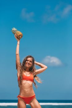Woman in a red bikini enjoying summer, holding pineapple at the beach.