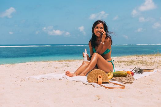 Woman relaxing on a sandy beach with picnic items, enjoying the sun and ocean view.