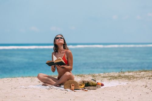 Free Woman in bikini reading a book on a sunny beach, enjoying summer vacation. Stock Photo