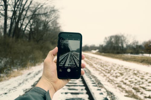 Free Person Holding Iphone Taking Photo of Train Rails Stock Photo