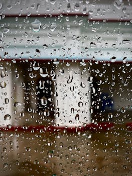 Close-up view of raindrops on glass, creating a textured effect with a blurred backdrop.