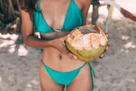 穿着绿松石比基尼的女人在沙滩上拿着一颗新鲜的椰子