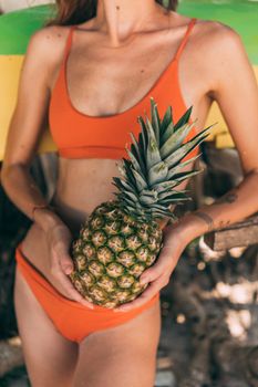 Woman in orange bikini holding a pineapple against tropical background. Perfect for summer and vacation themes.