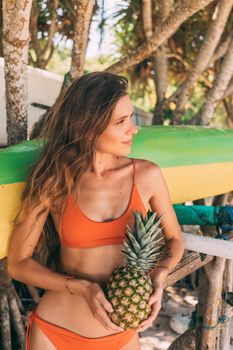 Young woman in a bikini holding a pineapple, enjoying a tropical vacation outdoors.