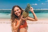 一个快乐的女人享受在阳光明媚的热带海滩度假，而持有一个成熟的菠萝