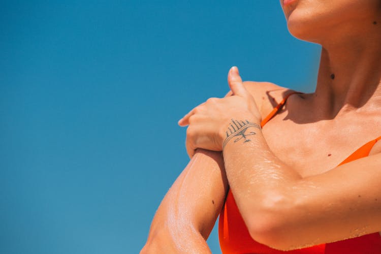 Woman Wearing An Orange Swimsuit Applying Sunscreen