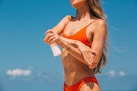 身穿橙色比基尼的女子在阳光明媚的海滩上涂抹防晒霜