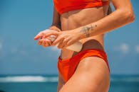 穿着比基尼的女人涂抹防晒霜，拍摄于阳光明媚的天空和海洋背景下