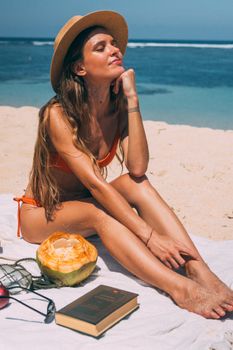 Woman in bikini enjoys sun on beach with a coconut and book. Perfect for summer vacation imagery.