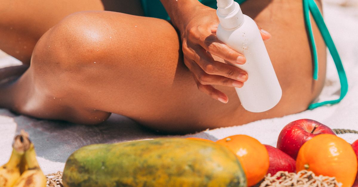 Photo by Mikhail Nilov A sunbather applies sunscreen on the beach with tropical fruits nearby.