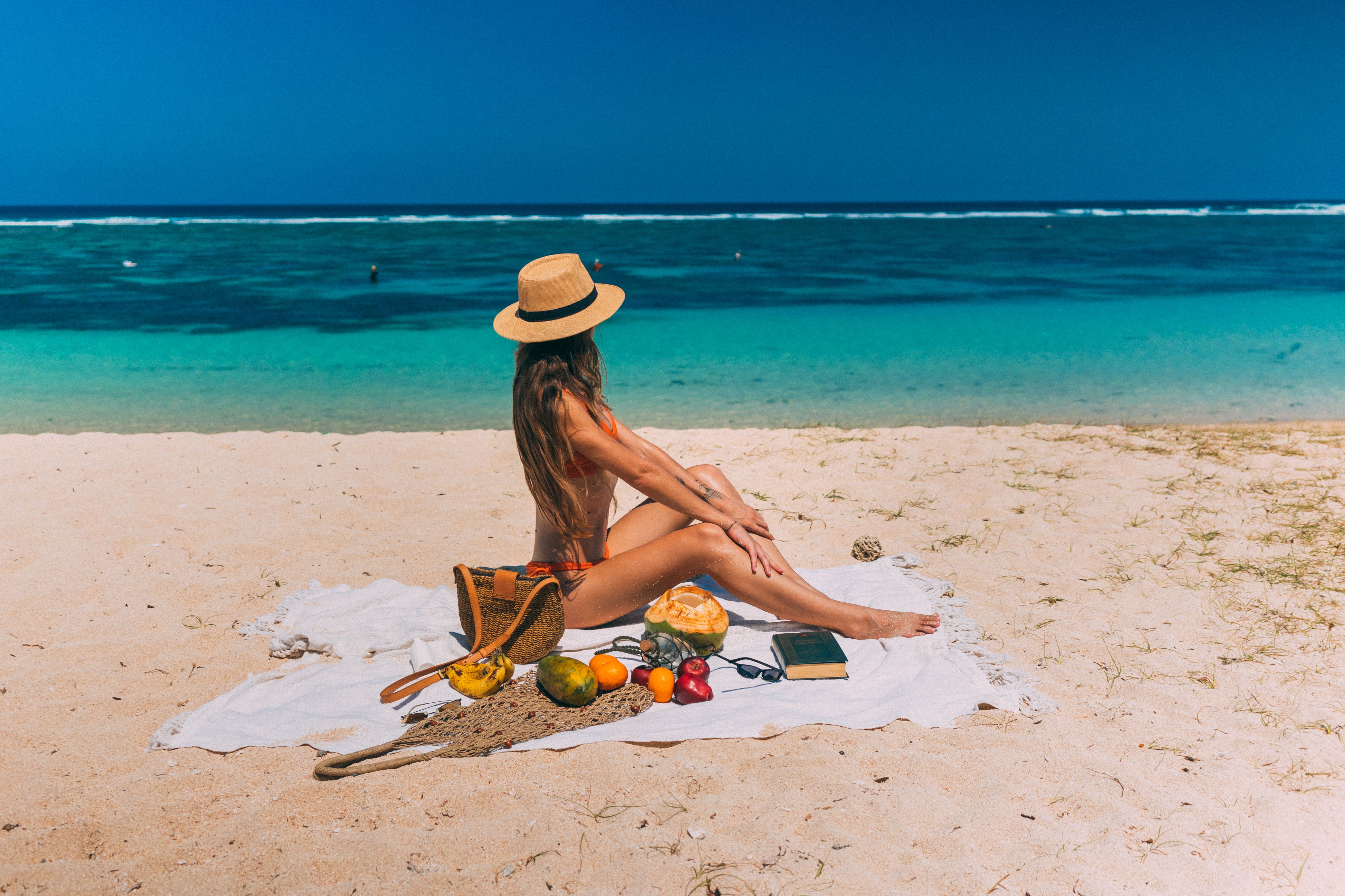Sunscreen bottle, wide-brimmed hat, and sunglasses on a beach towel