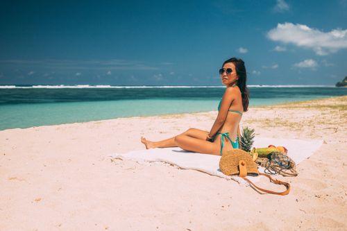 Free Woman in swimwear relaxing on a tropical beach with fruits, enjoying a sunny day. Stock Photo