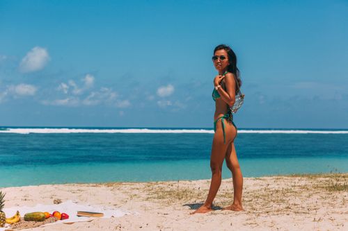 Free Woman in bikini on sandy beach with tropical fruits and clear ocean in background. Stock Photo