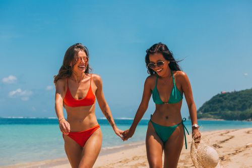 Free Two women in bikinis enjoying a sunny day on a sandy beach. Stock Photo
