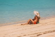 一名女子戴着草帽，穿着比基尼，在沙滩上放松身心，享受海边阳光明媚的夏日