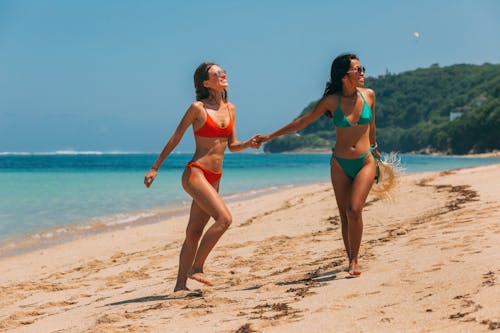 A Pair of Women in Bikinis Walking on Beach Shore Holding Hands