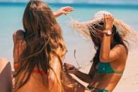 两名穿着比基尼、戴着太阳帽的女子在海滩上享受阳光明媚的一天