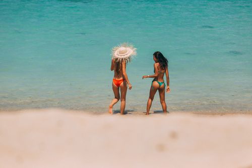 Free Two women in bikinis enjoying a sunny day on the beach by the clear blue ocean. Stock Photo