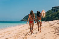 夏日阳光下，两名穿着泳衣的女子在沙滩上散步的令人愉快的场景