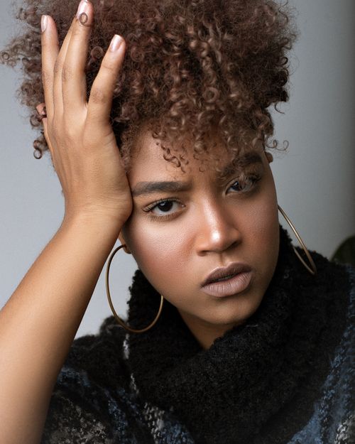 Free Stylish African American female with makeup and Afro hairstyle touching head while looking at camera on gray background Stock Photo
