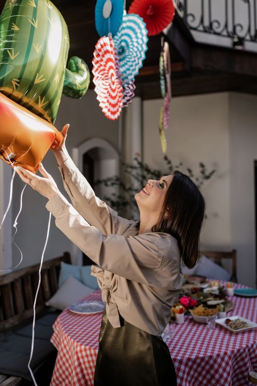 Free Young woman enjoying an outdoor party, holding decorative balloons under colorful hanging ornaments. Stock Photo