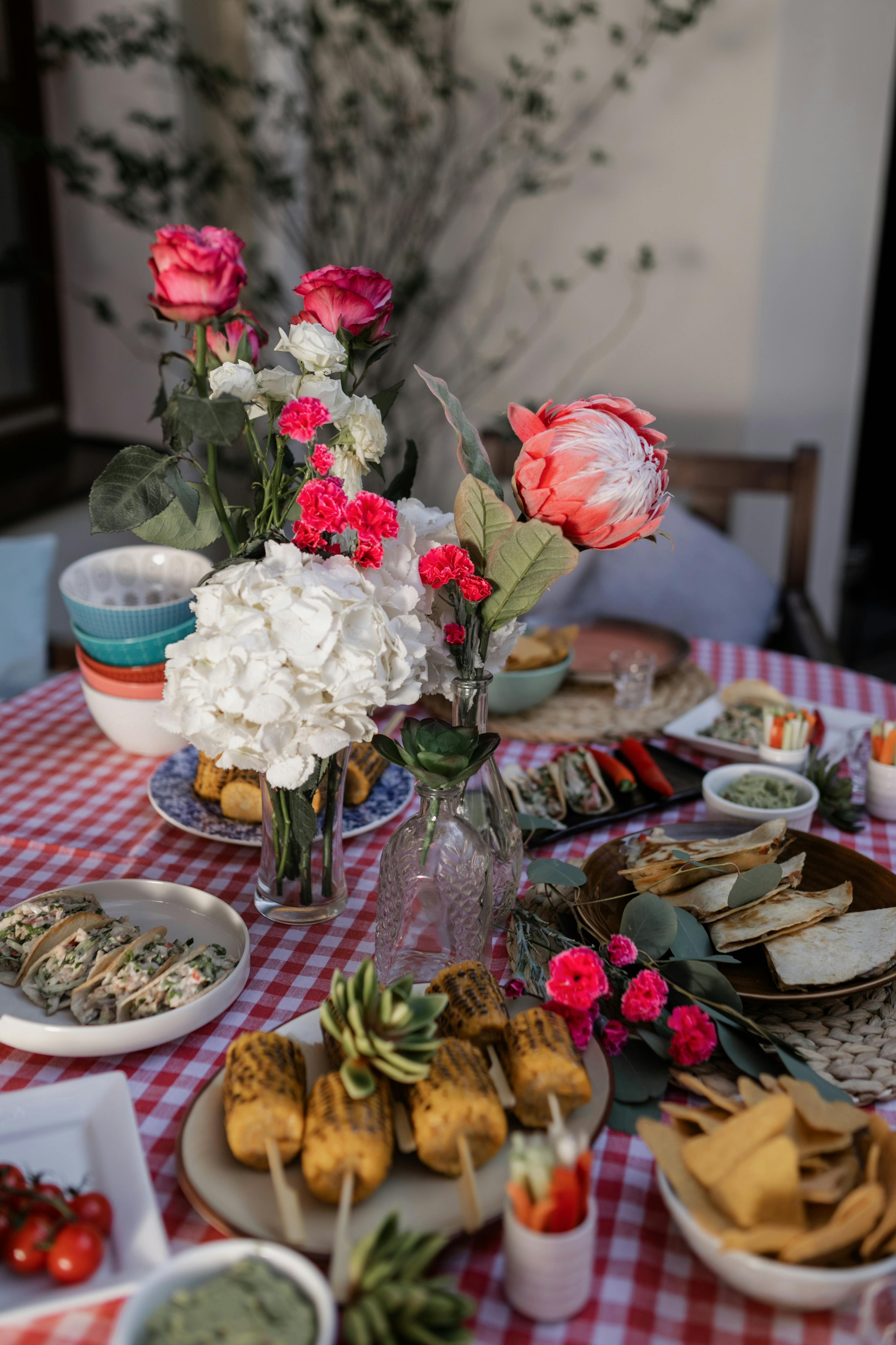 food on table beside red and white flowers in clear glass vase