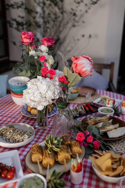 Food on Table Beside Red and White Flowers in Clear Glass Vase