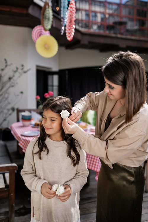 Free A woman adjusts a young girl's hair with a white flower at an outdoor family event. Stock Photo