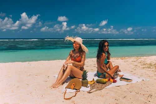 Free Two women enjoying a sunny beach picnic with fruits by the sea. Perfect summer relaxation scene. Stock Photo