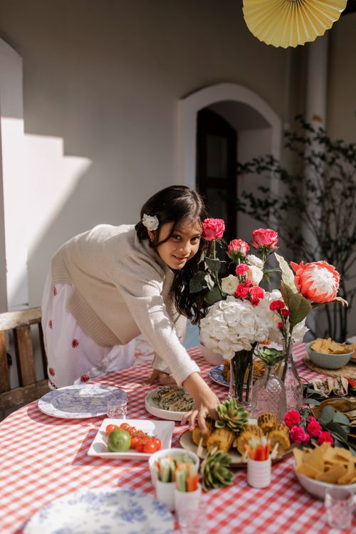 Free A cheerful child reaches for food at a vibrant table set for a festive occasion, surrounded by flowers. Stock Photo