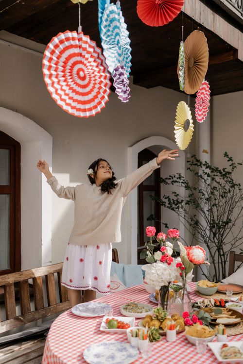 Free Teen girl enjoying an outdoor celebration with vibrant paper decorations and a feast. Stock Photo
