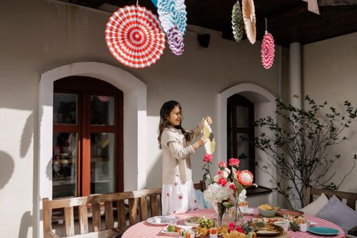 Free A woman decorates an outdoor party table with flowers and colorful hanging ornaments. Stock Photo