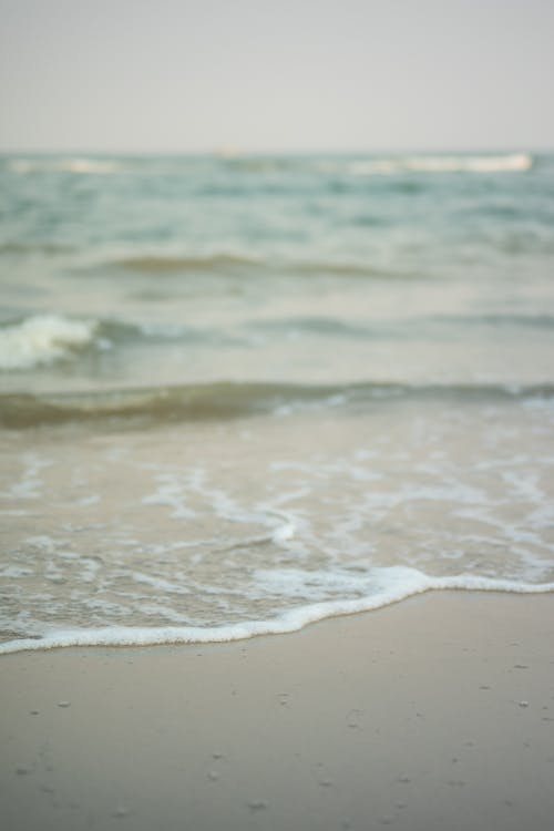 Scenery view of ocean with foamy water fluids on sandy coast in daytime on blurred background