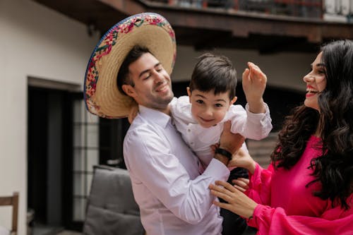 Man in White Dress Shirt with Sombrero Carrying a Boy Beside Woman in Pink Dress