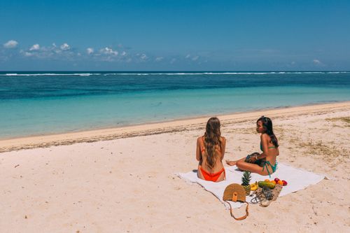 Free Two women in swimsuits enjoying a sunny day on a tropical beach with clear blue waters. Stock Photo