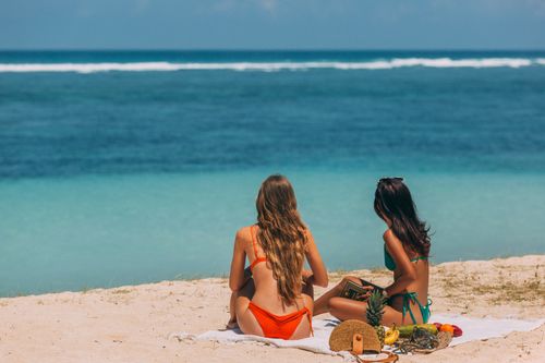 Free Two women enjoying a sunny day on a tropical beach, relaxing with a beautiful ocean view. Stock Photo