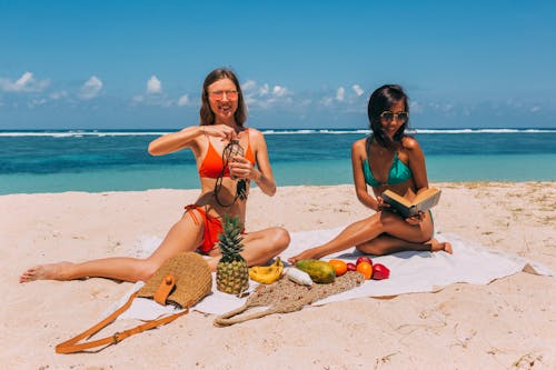 Happy Women in Bikinis Sitting on Blanket on Beach