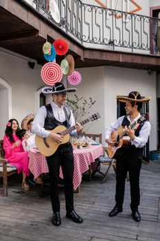 Two men in sombreros playing guitars at a lively Mexican celebration outdoors.
