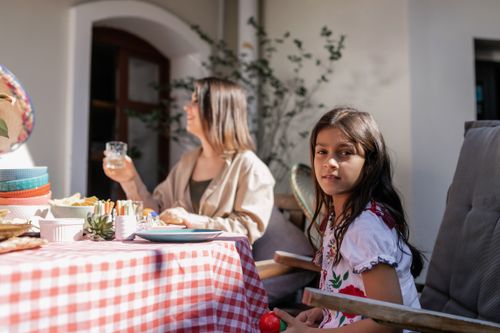 Free A young girl and woman enjoying an outdoor picnic under the sunlight with food and drinks. Stock Photo