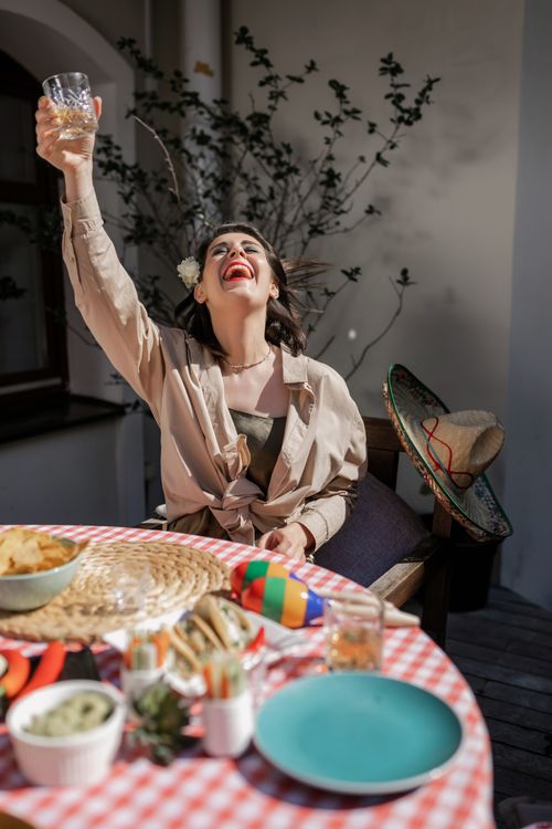 Free A woman joyously raises her glass at a vibrant festive table with maracas and sombrero. Stock Photo