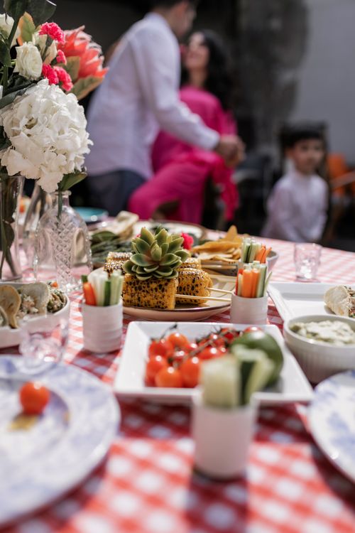 Free A colorful outdoor family gathering featuring fresh vegetables and flowers on a red checkered tablecloth. Stock Photo