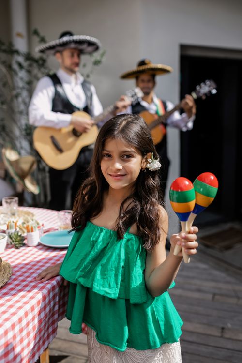 Free A young girl holds maracas during a festive Mexican celebration with musicians. Stock Photo