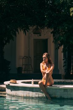Woman in a bikini sitting by a poolside in a relaxed summer setting.