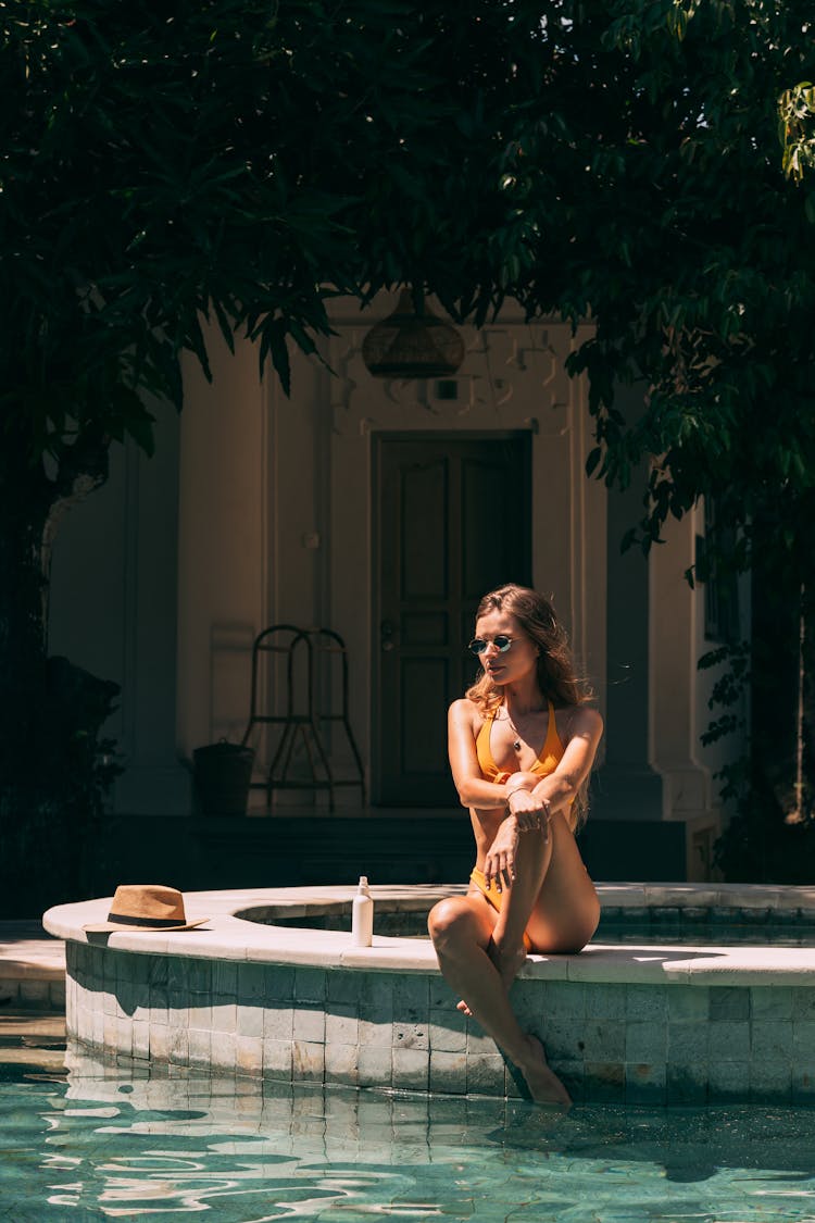 A Woman In Bikini Sitting By The Poolside