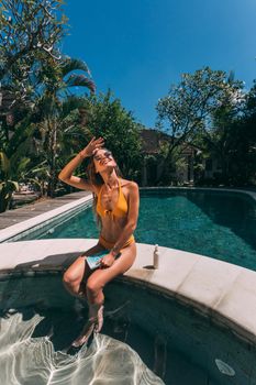 A woman relaxing by the pool in a bikini enjoying the sunny summer day.