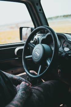 View of a tattooed man's arm and a Jeep's interior, captured on a sunny day.