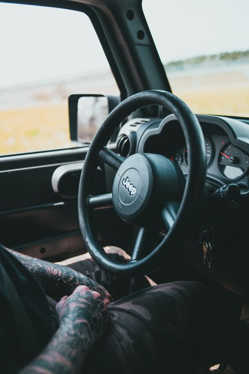 Free View of a tattooed man's arm and a Jeep's interior, captured on a sunny day. Stock Photo