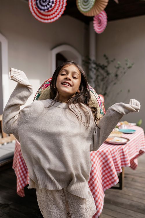 Free Smiling girl wearing a sweater enjoying a festive meal setting indoors, capturing joy and warmth. Stock Photo
