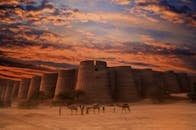 日落时分，沙漠中的古老堡垒景色令人惊叹，前景是骆驼和人